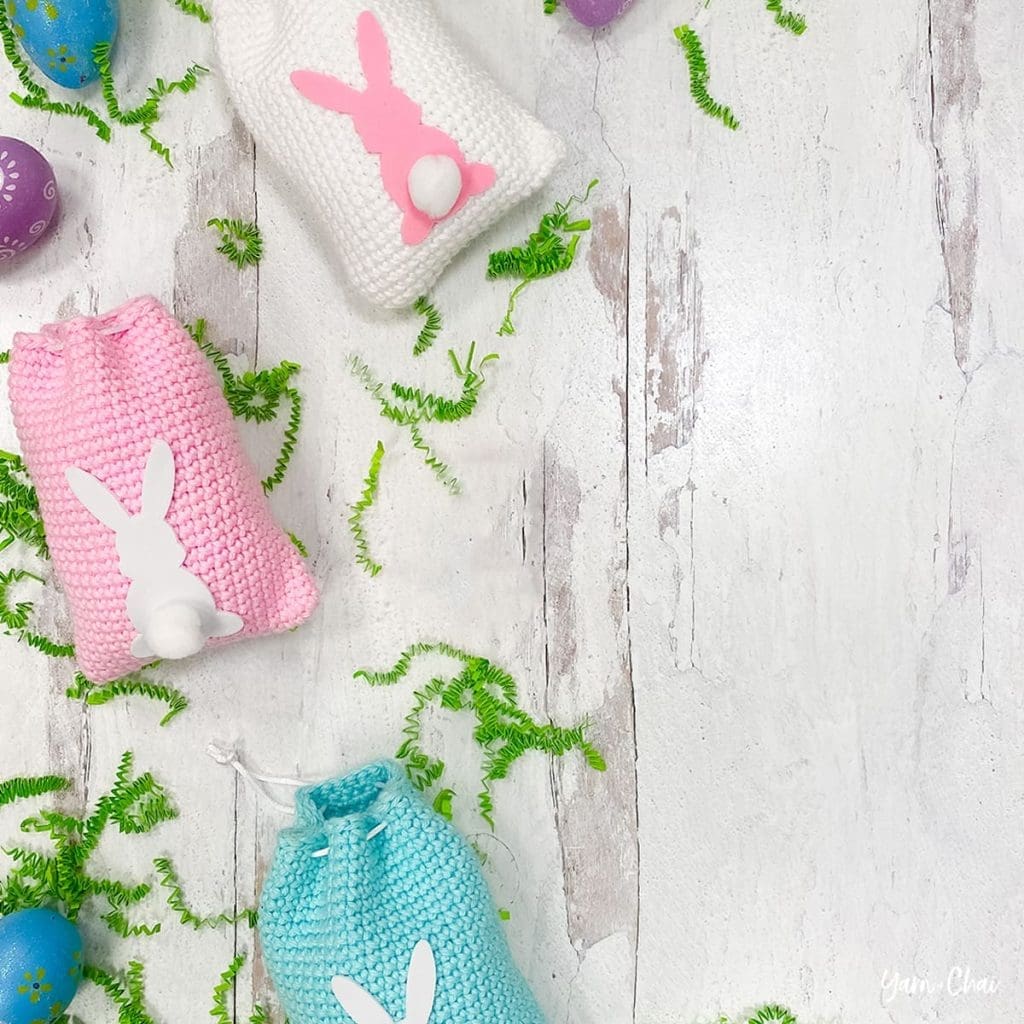 Three easter bunny treat bags surrounded by grass and colorful eggs
